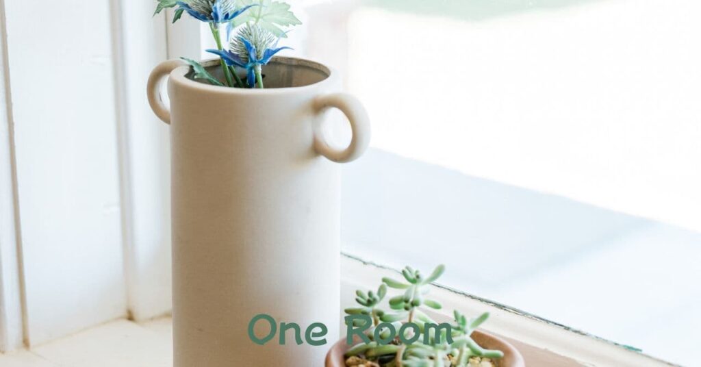 窓辺に置かれた白い花器と小さなグリーンの植物の写真 
