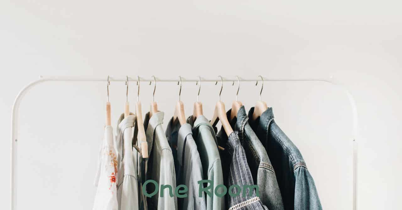 白い壁の前に整然と並んだ服と木製ハンガー。少ない服でも満足できる、シンプルで整ったクローゼットの状態を表現。